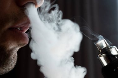 A man smokes an electronic cigarette, smoke and lips close-up, a man with a short beard.