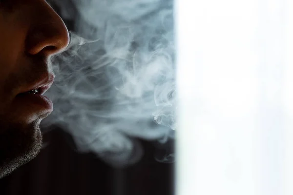 Male lips blowing smoke close-up, cigarette smoke and lips on black background, male unshaven and short beard.