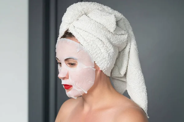 Home facial care, cloth mask on girl\'s face, girl wrapped in a towel.