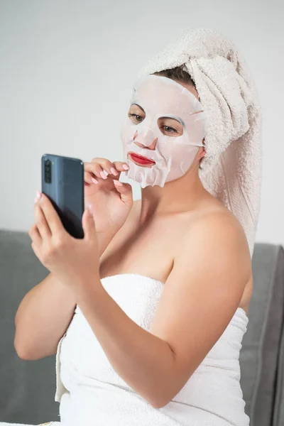 Facial skin cleansing procedure using a cosmetic mask, woman talking on the phone online, women\'s tricks and beauty.