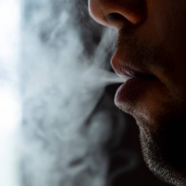 Seductive male lips blowing cigarette smoke, light stubble on beard, portrait of male lips and smoke on black background.