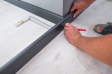 Wooden plinth in the room, installation of the plinth by a master carpenter, the master draws a pencil mark on the plinth.