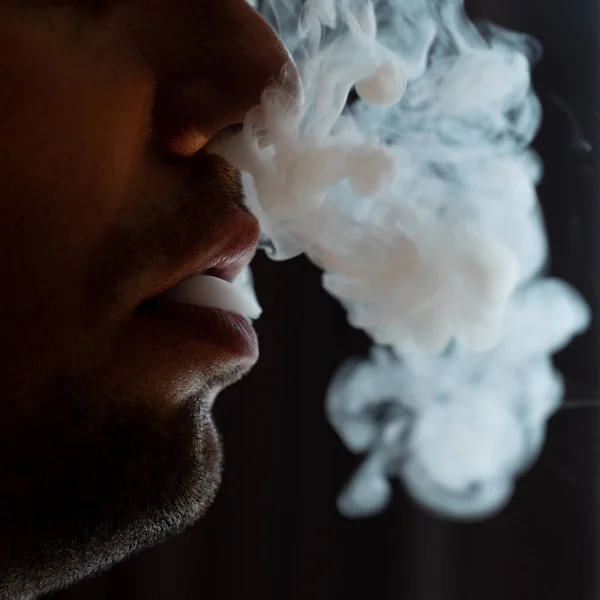 Male lips blowing smoke close-up, cigarette smoke and lips on black background, male unshaven and short beard.