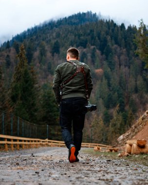 Orman yollarında yürürken, orman yolunda tek başına yürüyen bir adam sisli bir dağın arka planında, yol çitlerle çevrili..