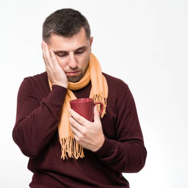 A handsome man touches his mouth with his hand with a pained expression because of a toothache or tooth disease, Dentist concept, a man wrapped in a scarf holds a mug in his hands.