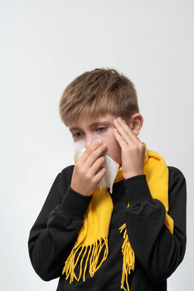 A child blows his nose into a napkin, children's seasonal diseases, a boy wrapped in a scarf, symptoms of the disease.