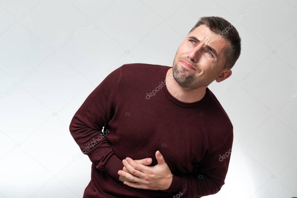 A man touches his stomach with two hands, on a white background with copy space, Stomach pain in a man, unbearable abdominal pain.