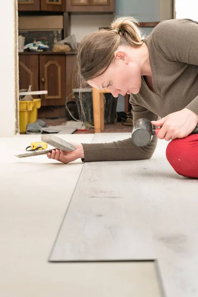 Quartz vinyl flooring and installation, a woman knocks a rubber hammer on the floor locks, repairs in the house.