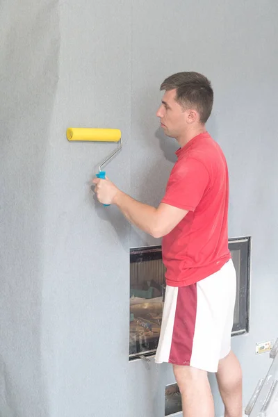 a worker glues wallpaper on a wall with a fireplace with the help of a rubber roller, repair work in the house.