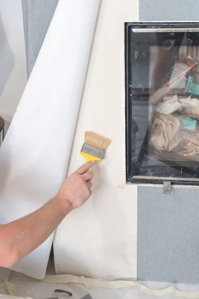 A person uses a brush to apply glue for wallpaper on the wall, repair work in the house, renovation of the wall.