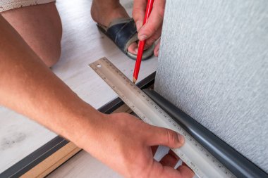 Installing a plinth in the room, measuring the required length using a square and a ruler, notching the plinth at the corner.