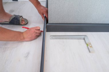The craftsman measures the length of the plinth for cutting, installing the plinth on the corner of the wall, close-up installation.