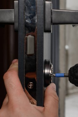 Bir iç kapının kilidi ve kapı kolu yerleştirilmiş, bir çilingir kapı ile çalışıyor, anahtarlar kapının kilidinde..