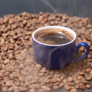 Kavrulmuş kahve ve koyu bir arka planda bir fincan kahve. Hafif buhar, bir fincan aromatik ve enerji içeceği..