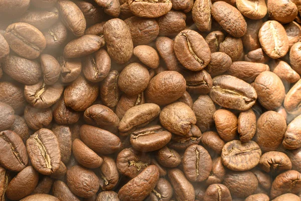 Black coffee beans with light smoke from steam, texture of coffee beans, copy space and place for writing.