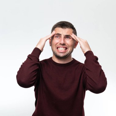 A handsome man wearing a casual sweater feels tired and has a headache, Stress and headache concept, severe headache, hands near the pulse of the head.