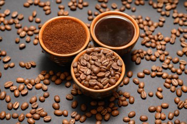 Üç fincan farklı kahve, kahve çekirdekleri, öğütülmüş ve hazır içecek, koyu arkaplana dökülmüş kahve çekirdekleri..