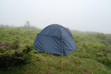 Lonely tent in the fog in the mountains, Carpathians of Ukraine and rest, dark blue tent.
