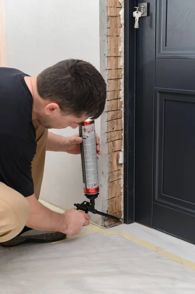 a man uses a spray gun with his hand and fills the gap with construction foam between a new wooden door and a wall, the process of installing a door.