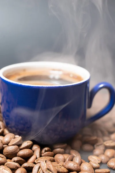 近くに豆が散乱したコーヒーカップ ホットコーヒーからの軽い蒸気 — ストック写真