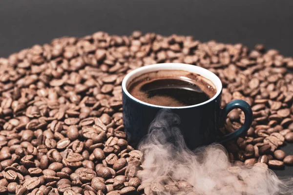 Roasted coffee and a cup of ready coffee on a dark background with light steam, a cup of aromatic and energy drink.
