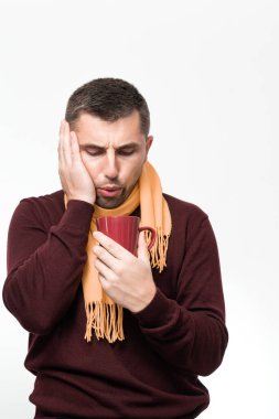 A handsome man touches his mouth with his hand with a pained expression because of a toothache or tooth disease, Dentist concept, a man wrapped in a scarf holds a mug in his hands.
