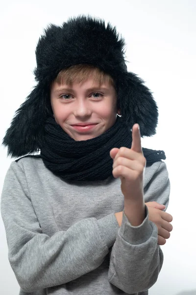 白い背景をした帽子 耳飾り スカーフの少年の肖像画 少年は彼の人差し指を上げています — ストック写真