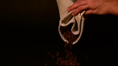 Bir adam kahve çekirdeklerini siyah arka planda küçük bir torbadan yavaş çekimde kahve döküyor..