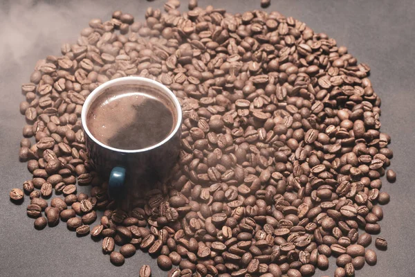 Roasted coffee and a cup of ready coffee on a dark background with light steam, a cup of aromatic and energy drink.