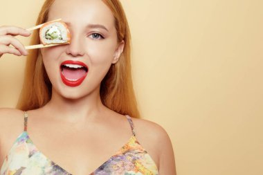 Güzel sarışın yemek çubuklarıyla suşi yer. Mesaj için yer, rulo ile poz veren bir model. Japon mutfağı restoranı. Turuncu arka planda gülümseyen ve gülen bir kadın.