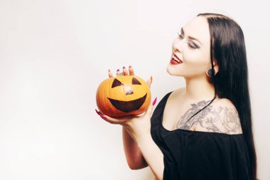 Muhteşem esmer bir cadı elinde bir balkabağı tutuyor ve Cadılar Bayramı 'nı kutluyor. Örümcek ağından yapılmış makyajlı ve kirpikli vampir kız.