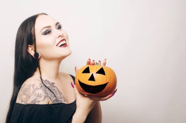 Muhteşem esmer bir cadı elinde bir balkabağı tutuyor ve Cadılar Bayramı 'nı kutluyor. Örümcek ağından yapılmış makyajlı ve kirpikli vampir kız.