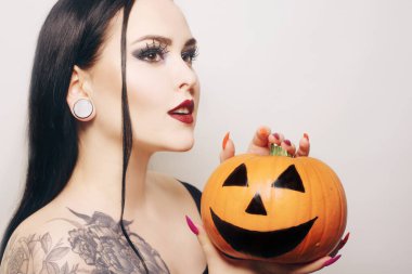 Muhteşem esmer bir cadı elinde bir balkabağı tutuyor ve Cadılar Bayramı 'nı kutluyor. Örümcek ağından yapılmış makyajlı ve kirpikli vampir kız.