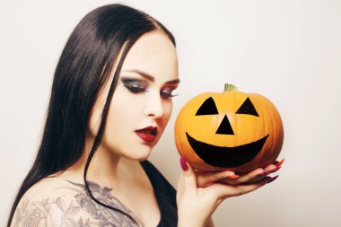 Muhteşem esmer bir cadı elinde bir balkabağı tutuyor ve Cadılar Bayramı 'nı kutluyor. Örümcek ağından yapılmış makyajlı ve kirpikli vampir kız.