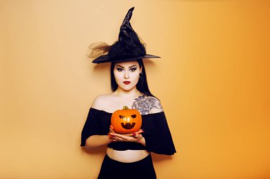 Elinde balkabağı tutan bir cadı kız, Cadılar Bayramı 'nı kutlayan bir kadın, kırmızı arka planda bir fotoğraf.