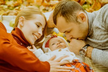 Birbirine aşık çift, sonbahar yaprakları üzerinde parka uzanmış, halının üzerine uzanmış, güzel bir sonbahar gününün tadını çıkarıyorlar. Mutlu, genç aile babası, anne ve küçük kız dışarıda eğleniyor.