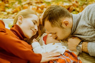 Birbirine aşık çift, sonbahar yaprakları üzerinde parka uzanmış, halının üzerine uzanmış, güzel bir sonbahar gününün tadını çıkarıyorlar. Mutlu, genç aile babası, anne ve küçük kız dışarıda eğleniyor.