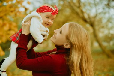 Anne ve kızı bir parkta sonbahar düşen yapraklar üzerinde güzel bir sonbahar günü zevk. Mutlu neşeli genç aile anne açık havada eğleniyor küçük bebeği ile. Uçan Bebek anne öpücüğü