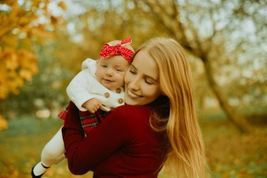 Anne ve kızı bir parkta sonbahar düşen yapraklar üzerinde güzel bir sonbahar günü zevk. Mutlu neşeli genç aile anne açık havada eğleniyor küçük bebeği ile. Uçan Bebek anne öpücüğü