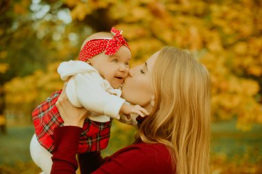 Anne ve kızı bir parkta sonbahar düşen yapraklar üzerinde güzel bir sonbahar günü zevk. Mutlu neşeli genç aile anne açık havada eğleniyor küçük bebeği ile. Uçan Bebek anne öpücüğü