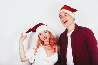 Kırmızı Noel Baba şapkalı bir çift beyaz arka planda gülüyor ve yeni yılı ve Noel 'i kutluyor. Pembe saçlı ve beyaz elbiseli kız gülüyor..