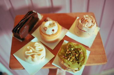 Pembe arka plandaki bir kalasın üzerindeki fırından gelen çeşitli tatlılar. Diyet ve tatlılar. Bir sürü lezzetli tatlı, güzel yuvarlak renkli pastalar.