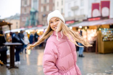 Şapkalı ve pembe ceketli hoş bir sarışın şehirde kış fuarlarında mı dolaşıyor? Noel gülüşü