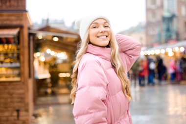 Şapkalı ve pembe ceketli hoş bir sarışın şehirde kış fuarlarında mı dolaşıyor? Noel gülüşü