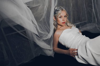 Gelinlik ve gümüş taç giymiş bir kız kanepede yatıyor. Sarışın kraliçe. Kameraya bakan bir mankenin moda fotoğrafı..