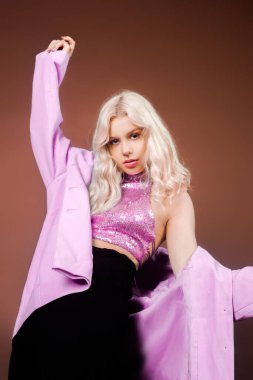 Pembe ceketli sarışın bir kadın, pullu bir ceket stüdyoda kahverengi arka planda poz veriyor. Yüksek moda, 90 'ların 80' leri. Kız dans ediyor ve hareket ediyor. Pembe makyajlı bir model