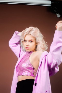Pembe ceketli sarışın bir kadın, pullu bir ceket stüdyoda kahverengi arka planda poz veriyor. Yüksek moda, 90 'ların 80' leri. Kız dans ediyor ve hareket ediyor. Pembe makyajlı bir model