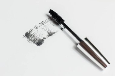 Mascara beyaz arka planda yatar ve fırçanın nasıl çalıştığını gösteren siyah bir iz bırakır. Kozmetik ürünleri ve makyaj malzemeleri.