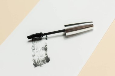 Mascara beyaz arka planda yatar ve fırçanın nasıl çalıştığını gösteren siyah bir iz bırakır. Kozmetik ürünleri ve makyaj malzemeleri.