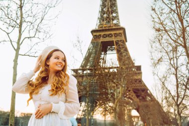 Paris 'teki Eyfel Kulesi' nin arka planında bereli ve kıvırcık saçlı bir elbise giymiş romantik bir yolculuk. Kadın gülüyor ve başka tarafa bakıyor..